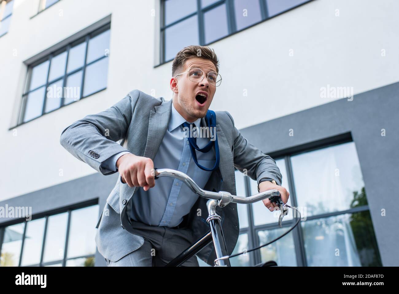 Un uomo d'affari eccitato in bicicletta vicino all'edificio all'aperto Foto Stock