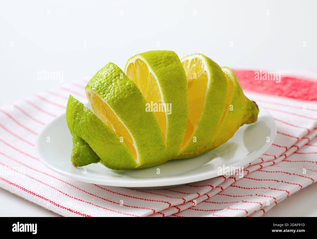 Limone con buccia verde e polpa gialla, affettato su piatto bianco Foto Stock