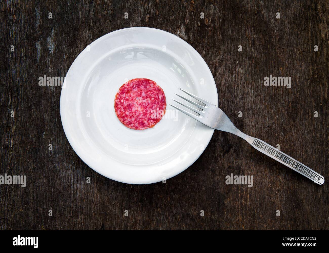 Un pezzo di salsiccia di salame nel piatto sul Grunge legno asse sfondo Foto Stock