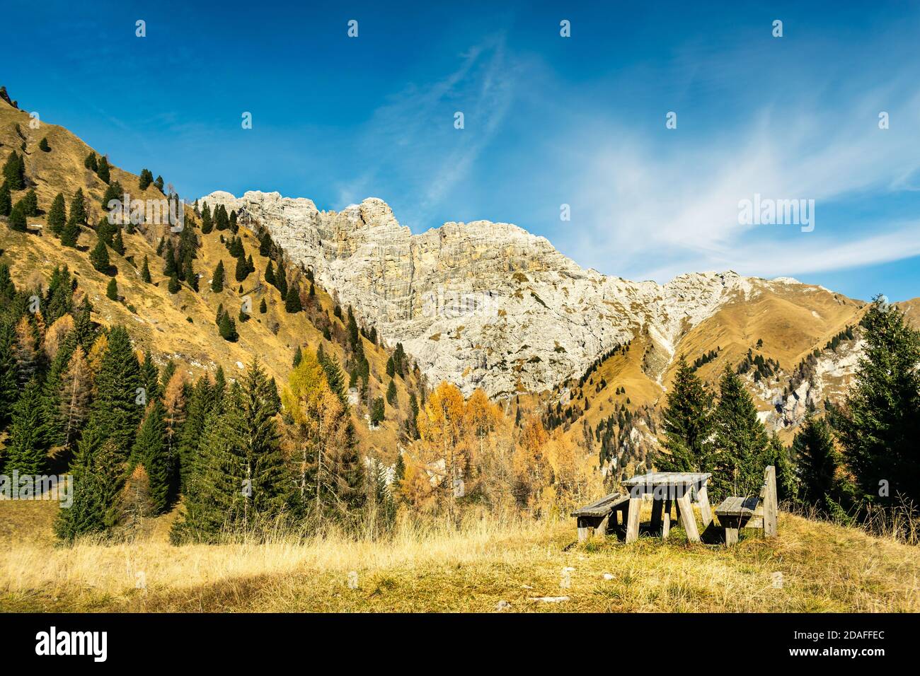 Panorama con cielo blu, montagne rocciose e pendii alberati. Sass de Mura e Monte Alvis. Nel tavolo in primo piano e panca di legno. Cesiomaggiore, Foto Stock