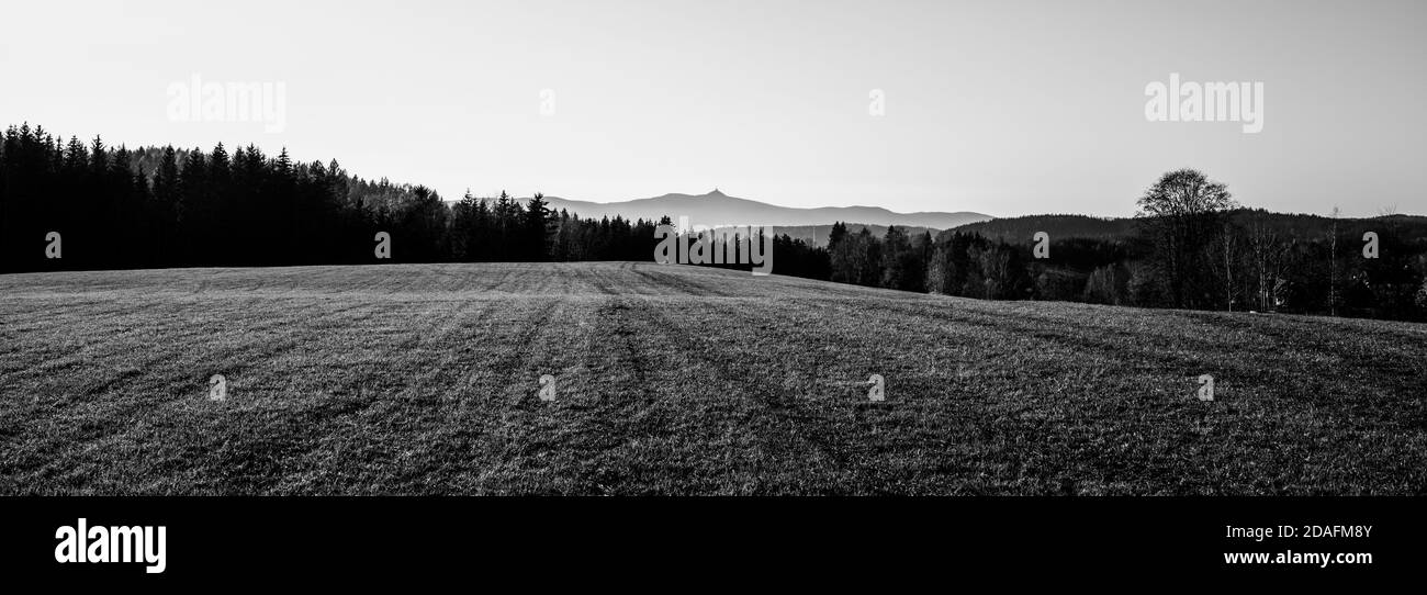 Montagna con hotel moderno e trasmettitore in cima. Soleggiato giorno d'autunno. Vista dal campo verde lontano. Repubblica Ceca. Immagine in bianco e nero. Foto Stock