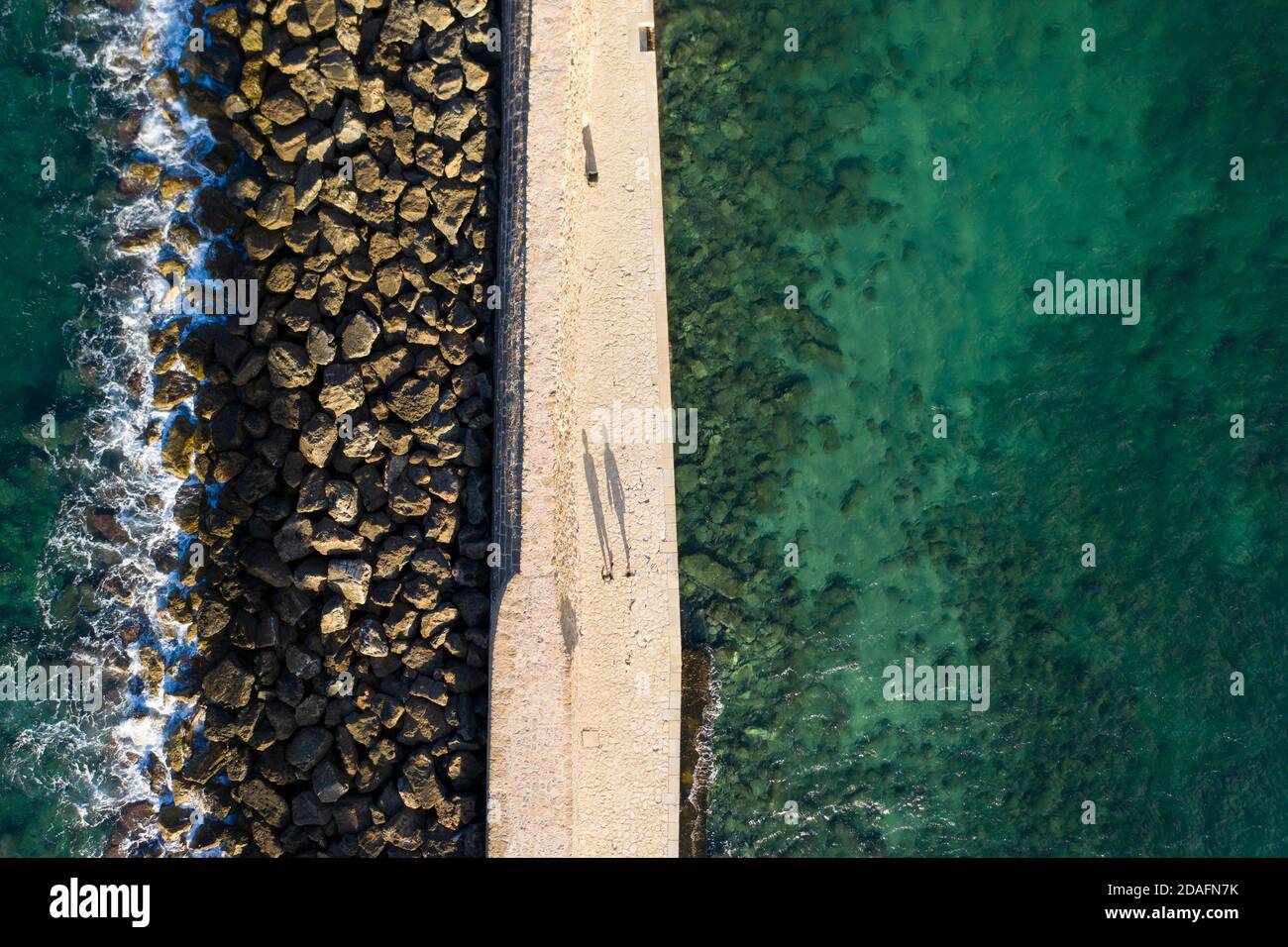 Vista aerea di due persone che gettano lunghe ombre sulla passerella per il faro nella città di Chania, Creta, Grecia Foto Stock