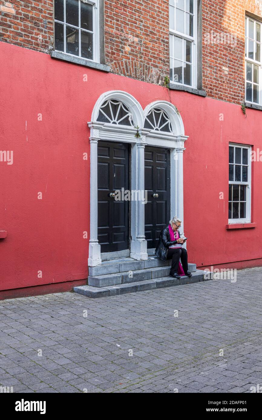 Siediti, seduto, Donna seduto sui gradini di una casa georgiana utilizzando il suo cellulare su St Kierans Street, Kilkenny, County Kilkenny, Irlanda Foto Stock