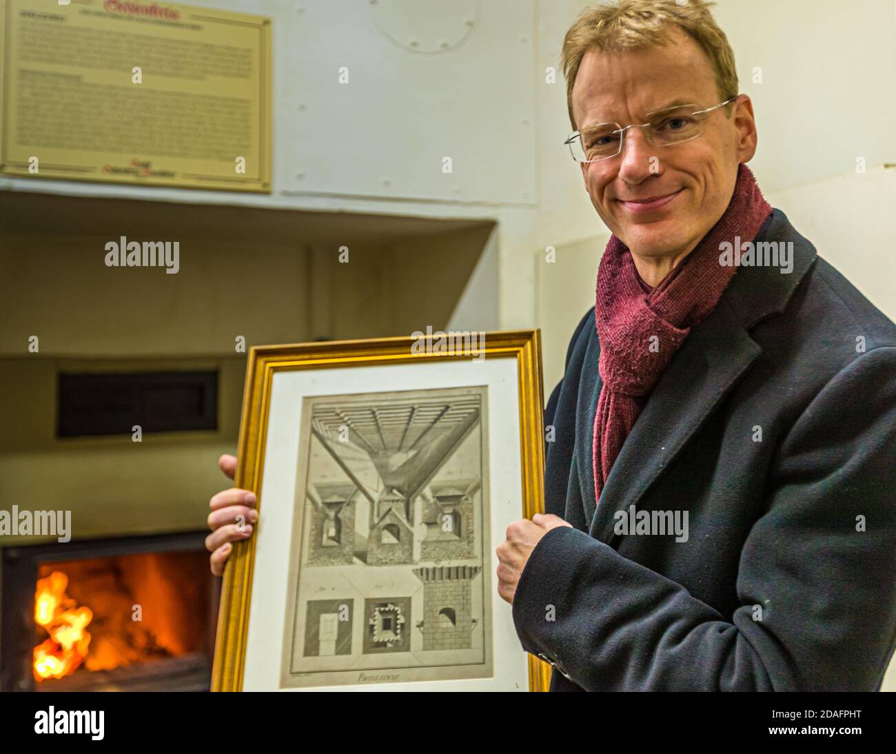 Matthias Trum di Schlenkerla Bräu nella generazione 6th della famiglia di fronte alla stufa a legna utilizzata per asciugare il malto verde. In mano tiene un disegno sull'essiccazione industriale del malto a base di Sir Nicholas Halse. Gli inglesi sono stati i primi a vietare il fumo dalla birra. Intorno al 1800 Georg Sedlmeyer, della fabbrica di birra Spaten di Monaco, costruì il primo forno non fumatori in Germania. Heller Brewery di Schlenkerla Smoke Beer Bamberg, Germania Foto Stock