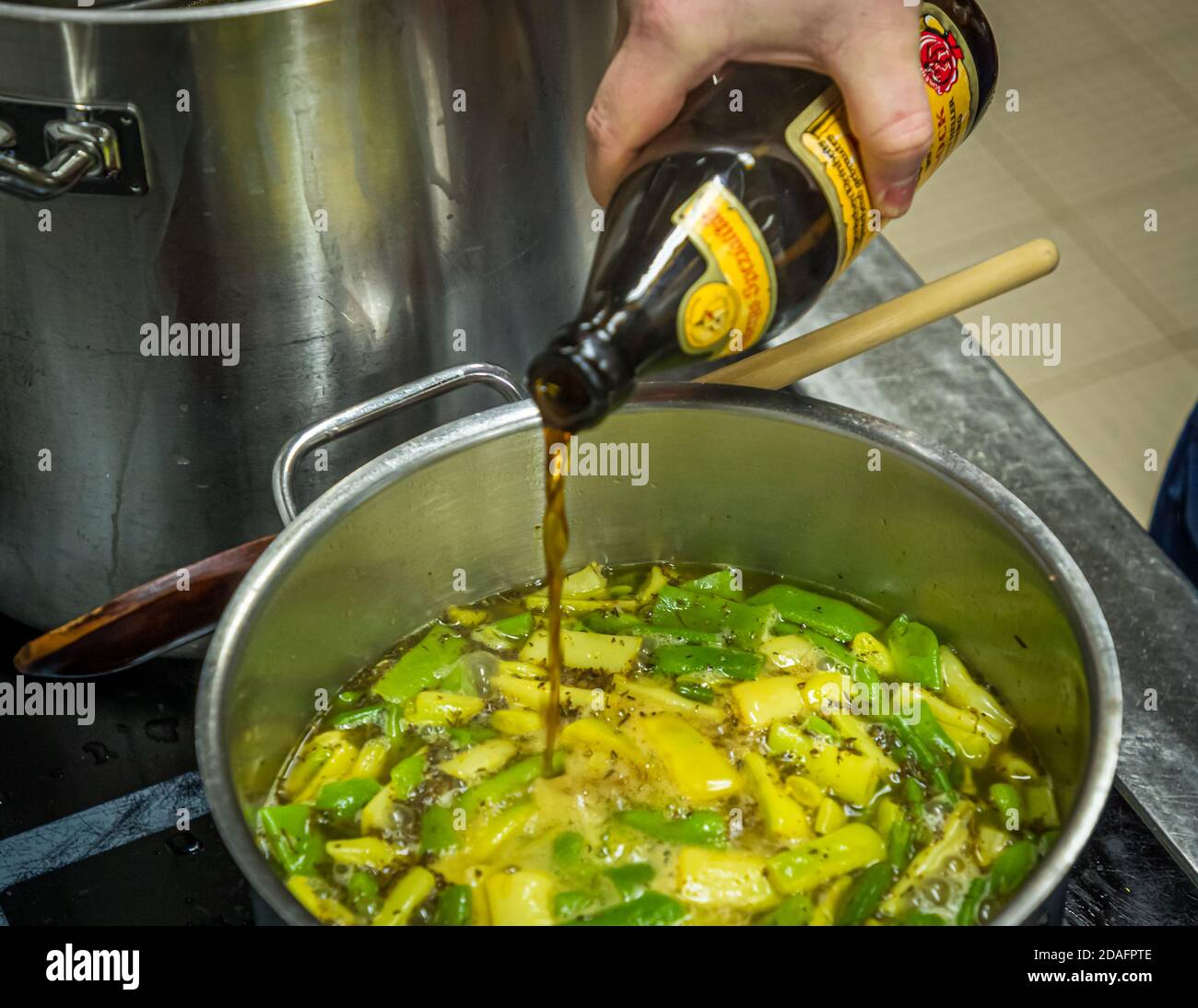 Simon Klein versa la birra affumicata Schlenkerla direttamente dalla bottiglia nella pentola di zuppa di fagioli nella cucina della birreria Heller-Bräu Schlenkerla a Bamberg, Baviera, Germania. Lo zafferano e le spezie sono già nel brodo. Foto Stock
