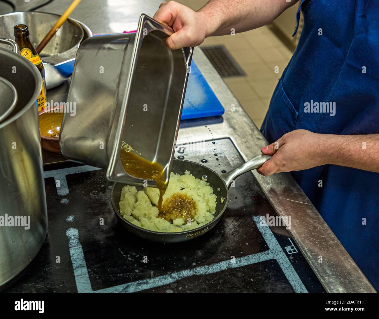 Simon Klein versa il liquido di liquirizia ridotto da un vassoio di metallo sulle cipolle sudate nella padella nella cucina della birreria Heller-Bräu Schlenkerla di birra affumicata a Bamberg, Bavaria, Germania. I tunks venivano serviti caldi e freddi nel Medioevo. Questa tunka Schlenkerla combina liquirizia di Bamberg, cipolle e majorana francica. Foto Stock