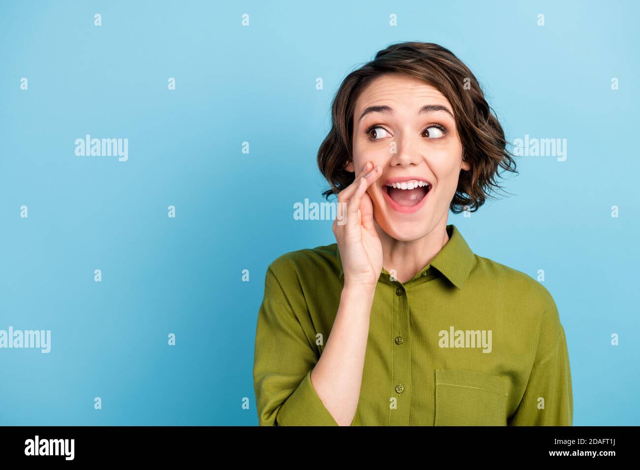 Ritratto fotografico di giovane bella ragazza con i capelli corti che dicono informazioni segrete rombo pettegolezzi indossando una camicia verde isolata su blu colore Foto Stock