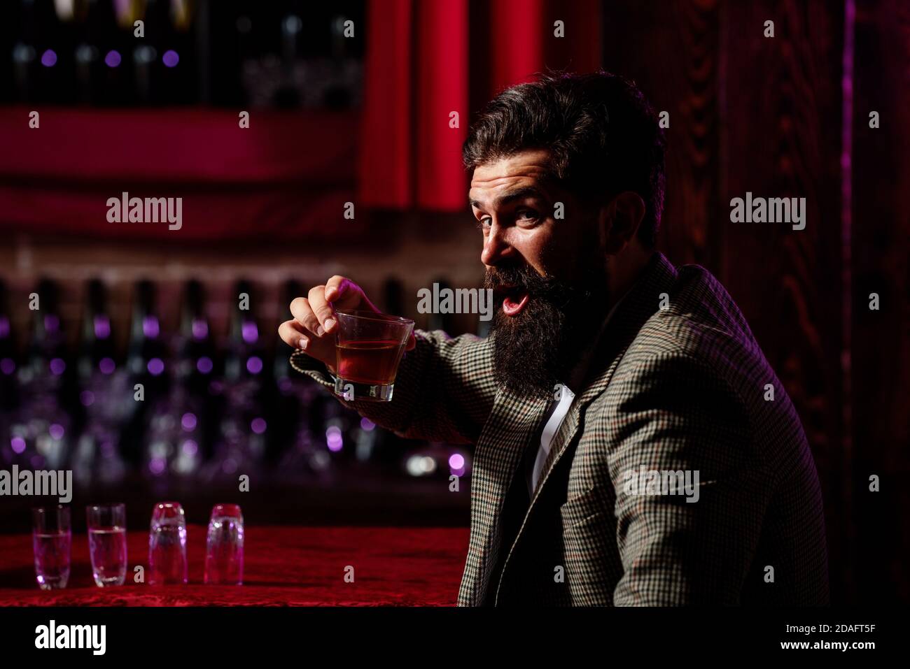 Uomo lavoratore vintage con barba lunga che tiene il whiskey. Seduto al bar. Foto Stock