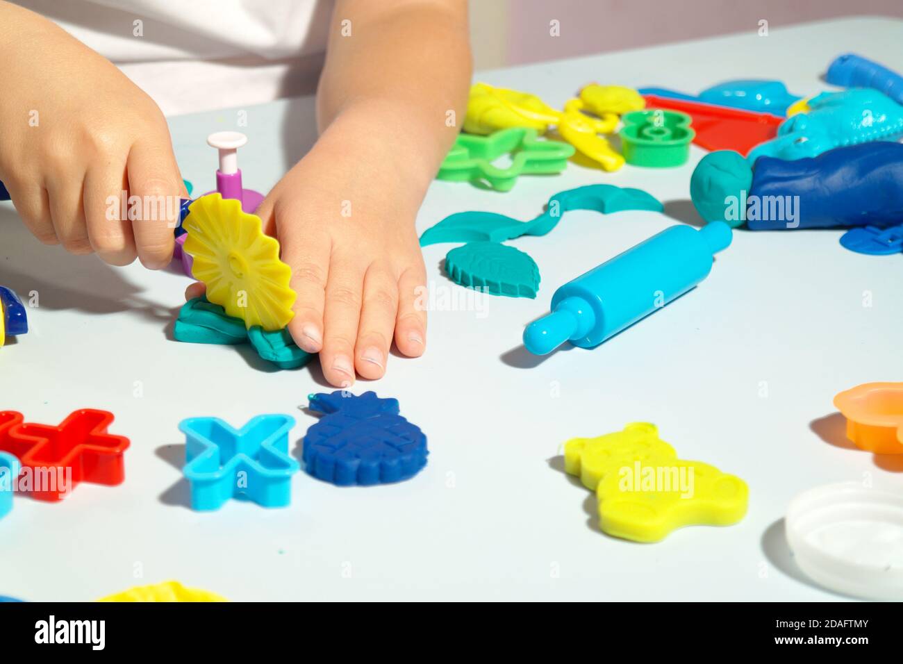 Il bambino gioca con l'impasto da gioco sul tavolo blu. Un sacco di giocattoli sul tavolo forme, rullo di pasta e forbici. Il bambino felice ha divertimento con i giocattoli. Foto Stock