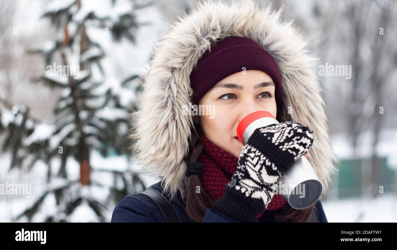 Bella giovane ragazza ama bere caffè da un thermos mentre cammina in un parco invernale. Foto Stock