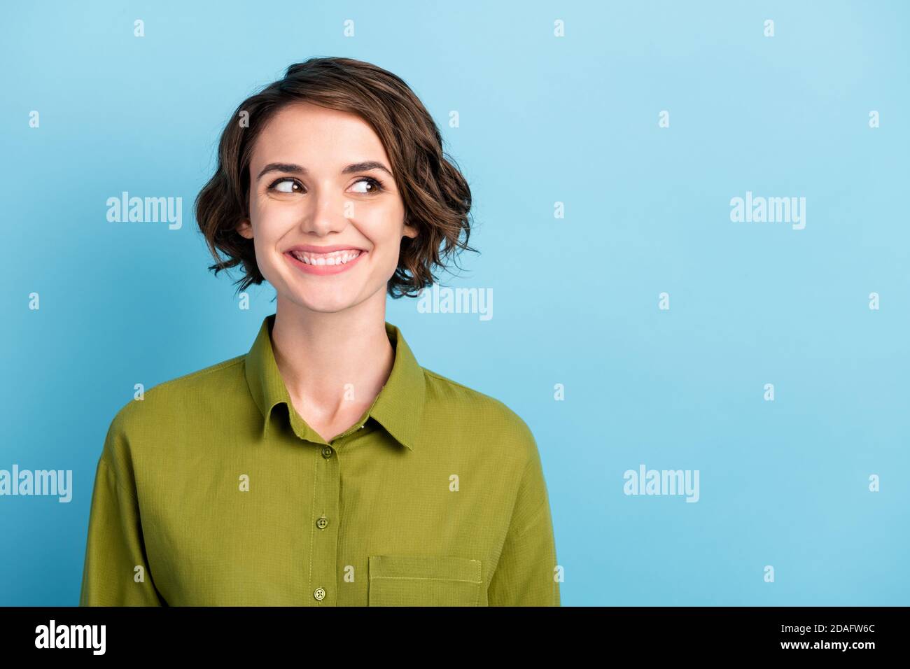 Ritratto fotografico di una divertente studentessa positiva con capelli ondulati e capelli corti indossando camicia verde sorridente ridendo guardando lato isolato su blu Foto Stock