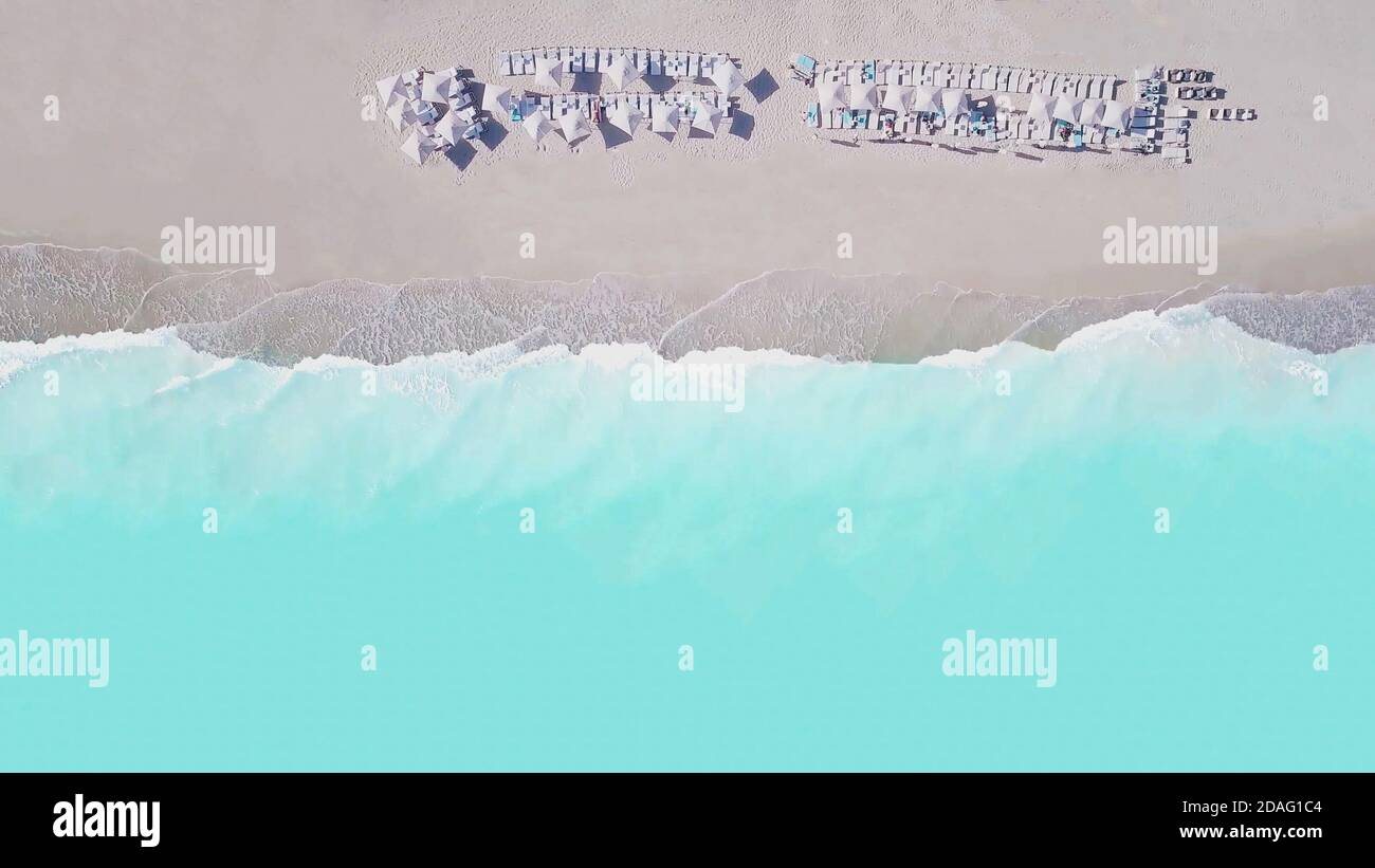 Vista aerea dall'alto della spiaggia di sabbia vuota e del mare turchese, con ombrelloni e lettini sulla sabbia bianca nella bella giornata estiva soleggiata. Foto Stock