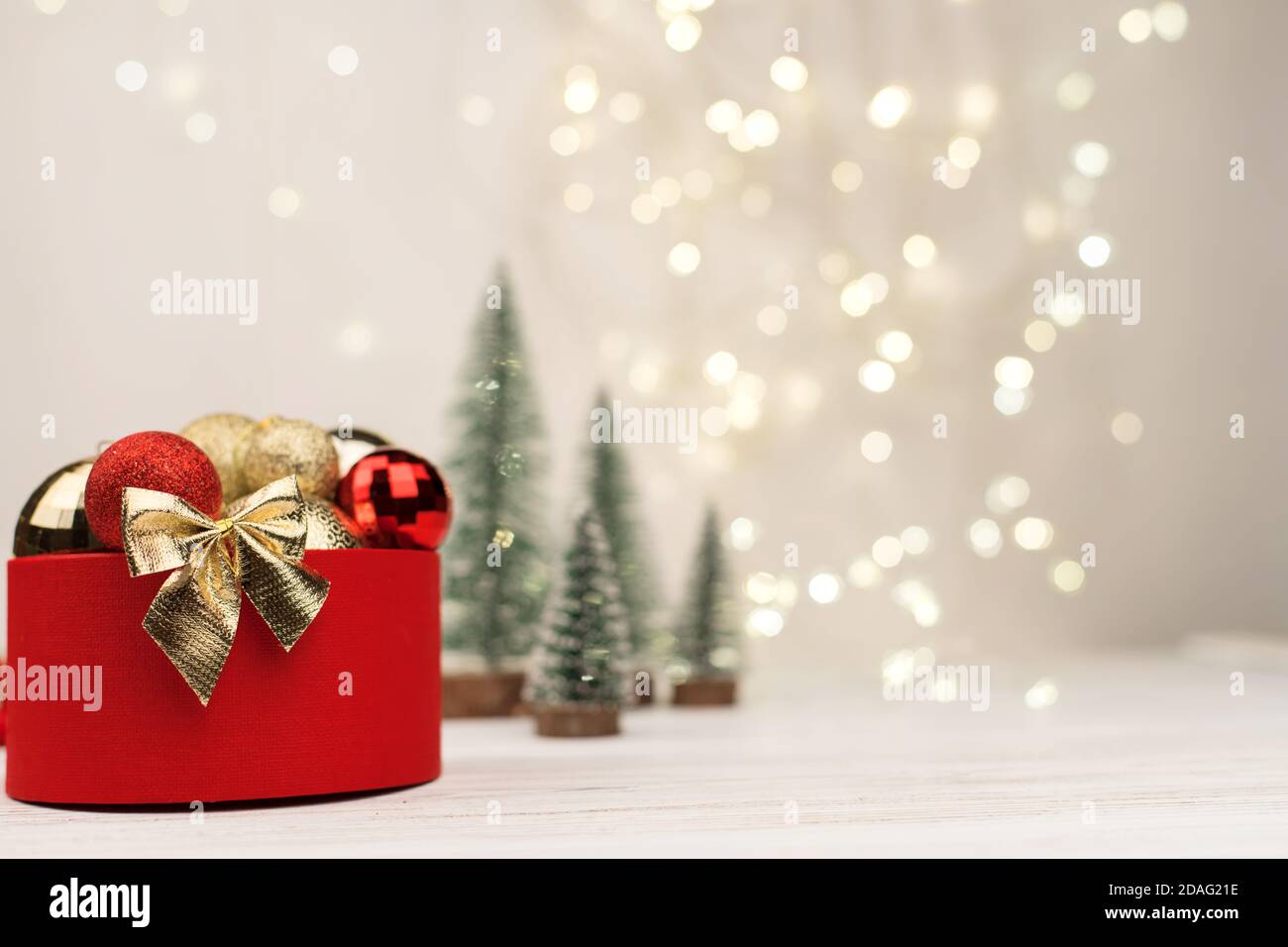 Scatola regalo di Natale rossa con un arco d'oro sullo sfondo di bokeh, alberi di Natale e giocattoli Foto Stock