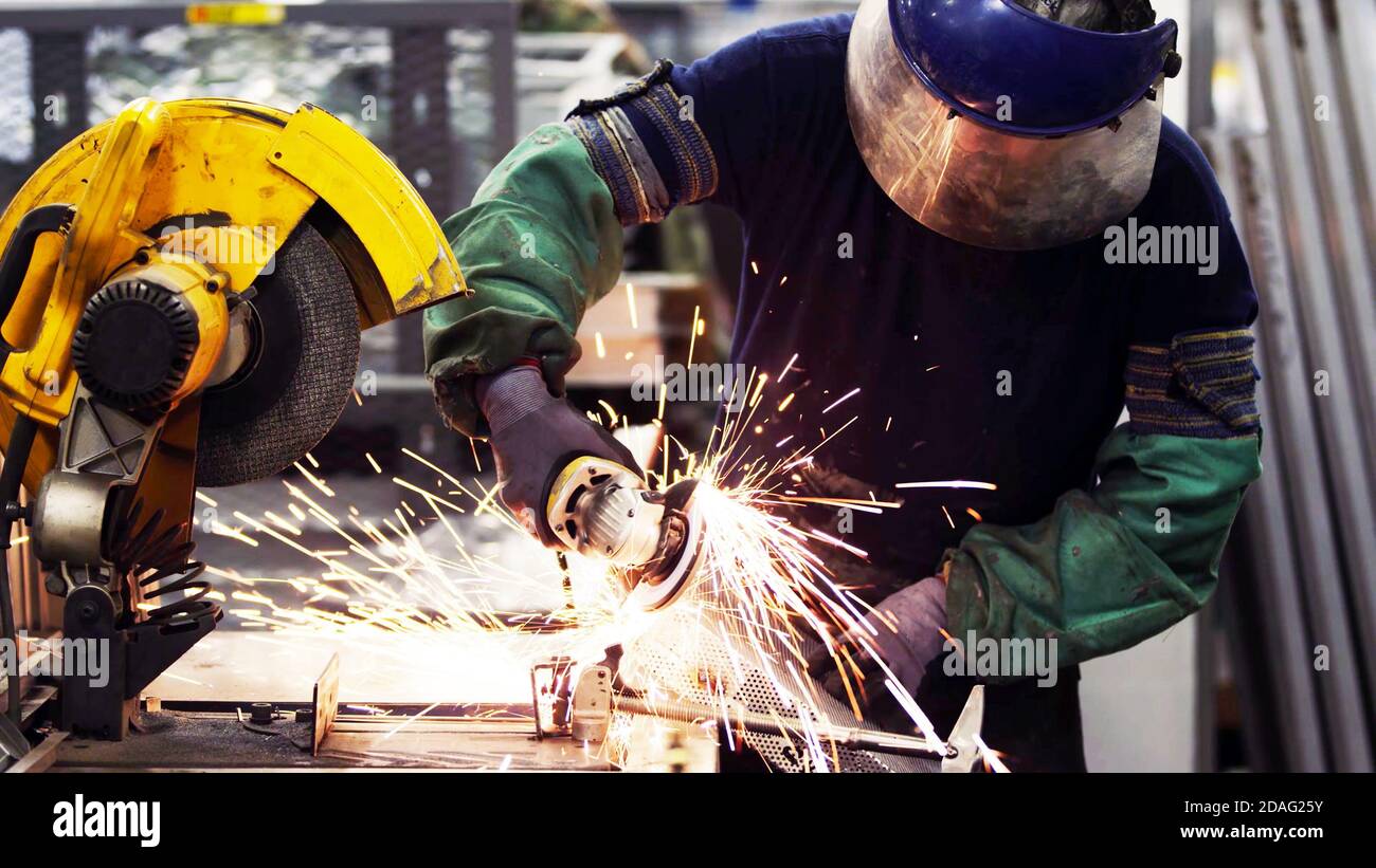 Lavoratori dell'industria pesante tagliano acciaio con rettificatrice in produzione industriale, indossando attrezzature di sicurezza Foto Stock