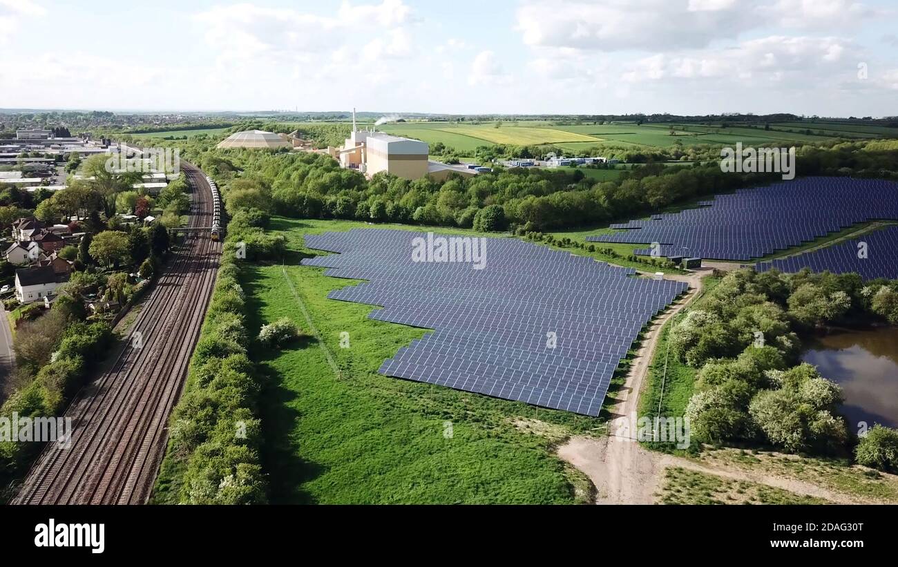 Vista aerea dei pannelli solari in campo verde accanto al treno ferroviario. Foto Stock