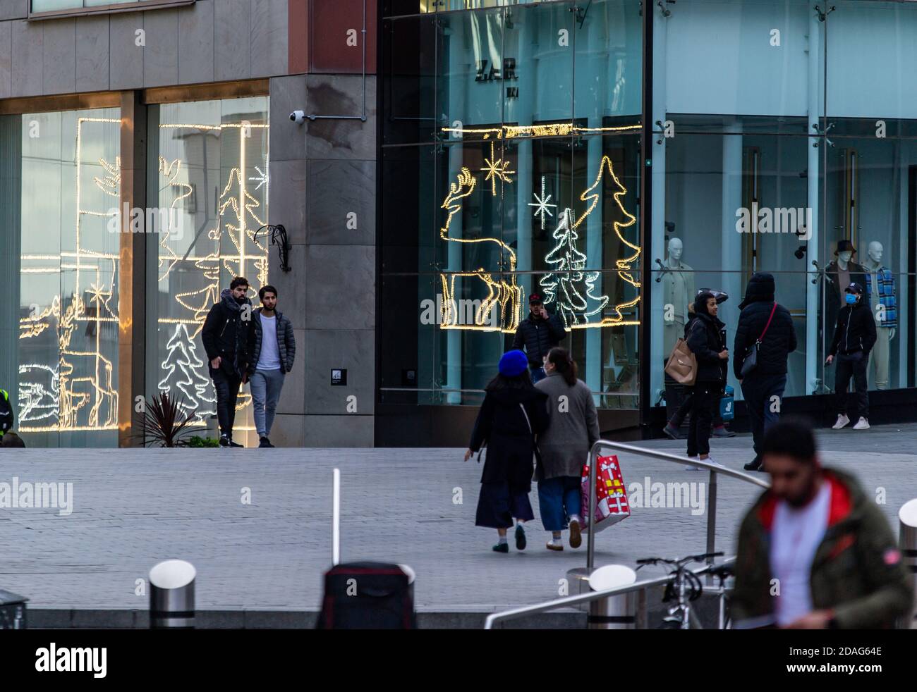 Gli amanti dello shopping all'arena di Birmingham, con le luci natalizie che si riflettono nelle vetrine dei negozi Foto Stock