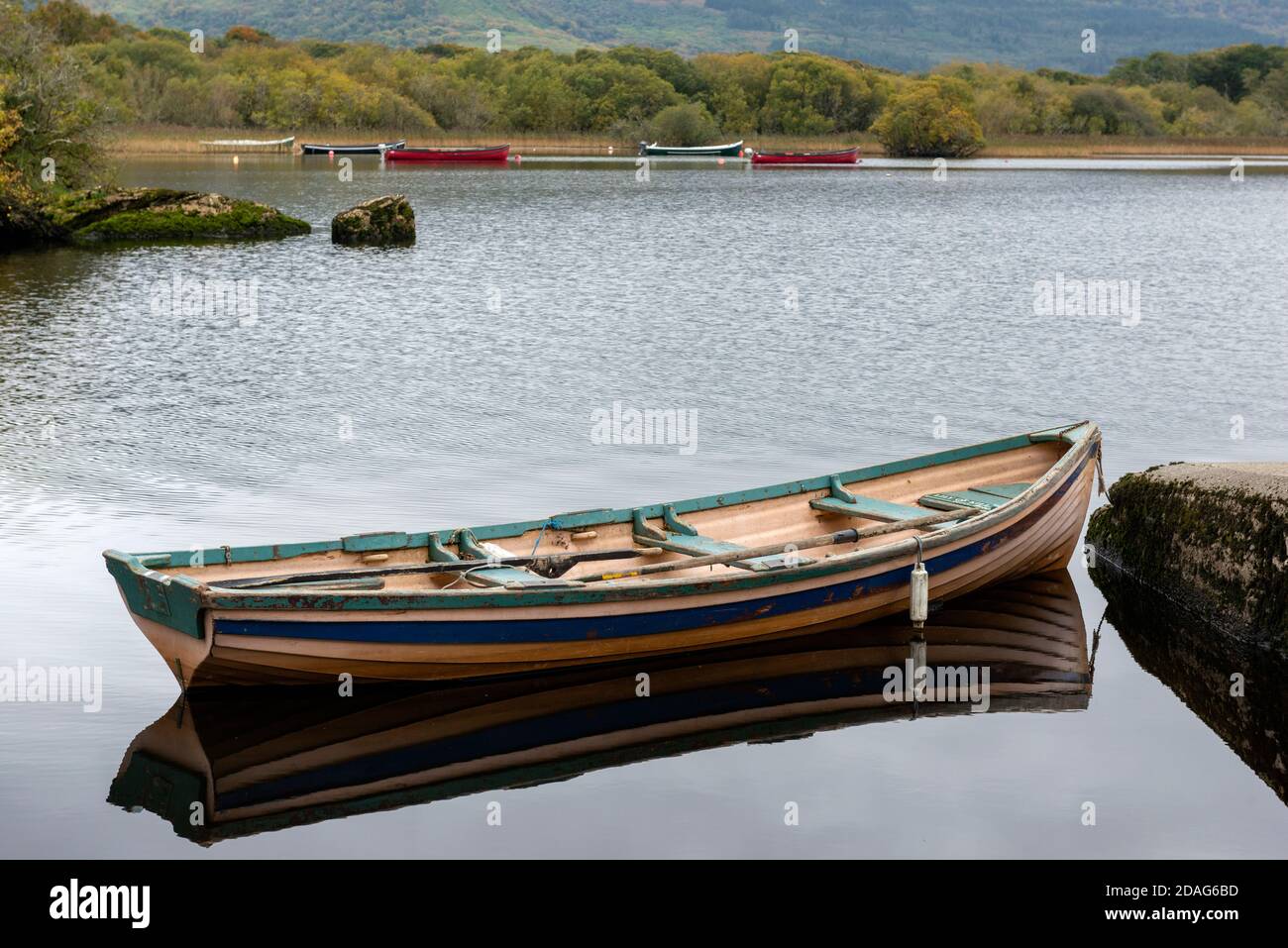 Piccola pesca o clinker barca sul lago calmo contro ormeggiate barche da pesca in lontananza nel Killarney National Park, County Kerry, Irlanda, Europa. Foto Stock