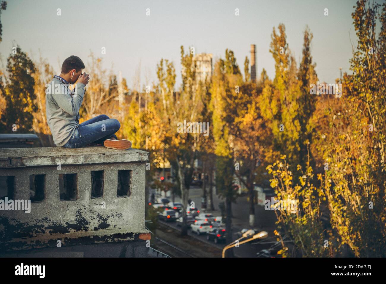 Giovane adolescente seduto su un tetto di un edificio e. fare foto dall'alto con una vecchia fotocamera Foto Stock