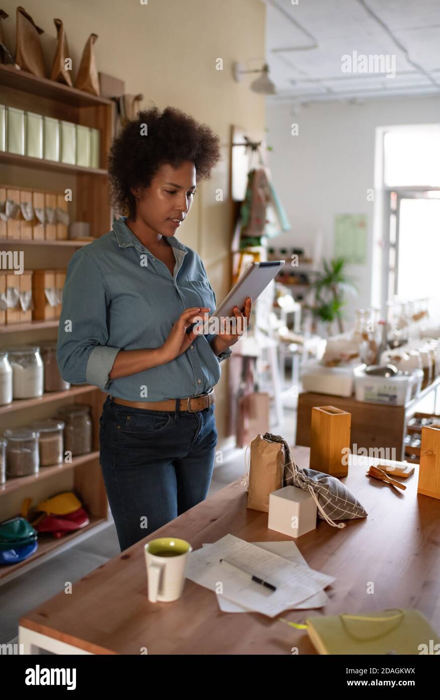 Donna nera che naviga tablet per la promozione del sito web durante il lavoro in negozio ecologico Foto Stock