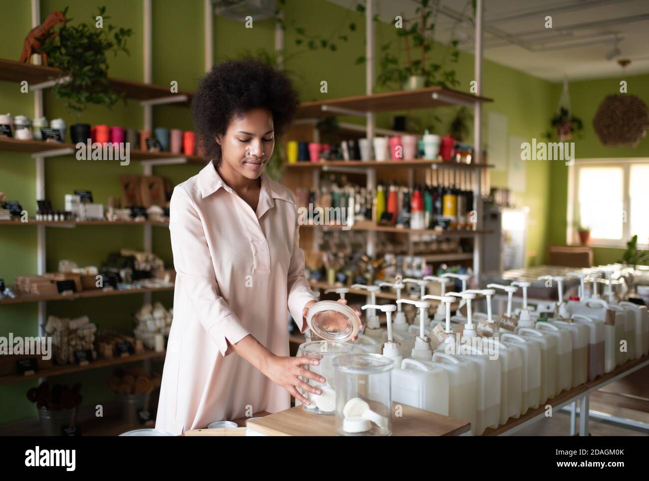 Venditore femminile nero che seleziona cosmetico organico mentre prepara l'ordine dentro negozio ecologico Foto Stock