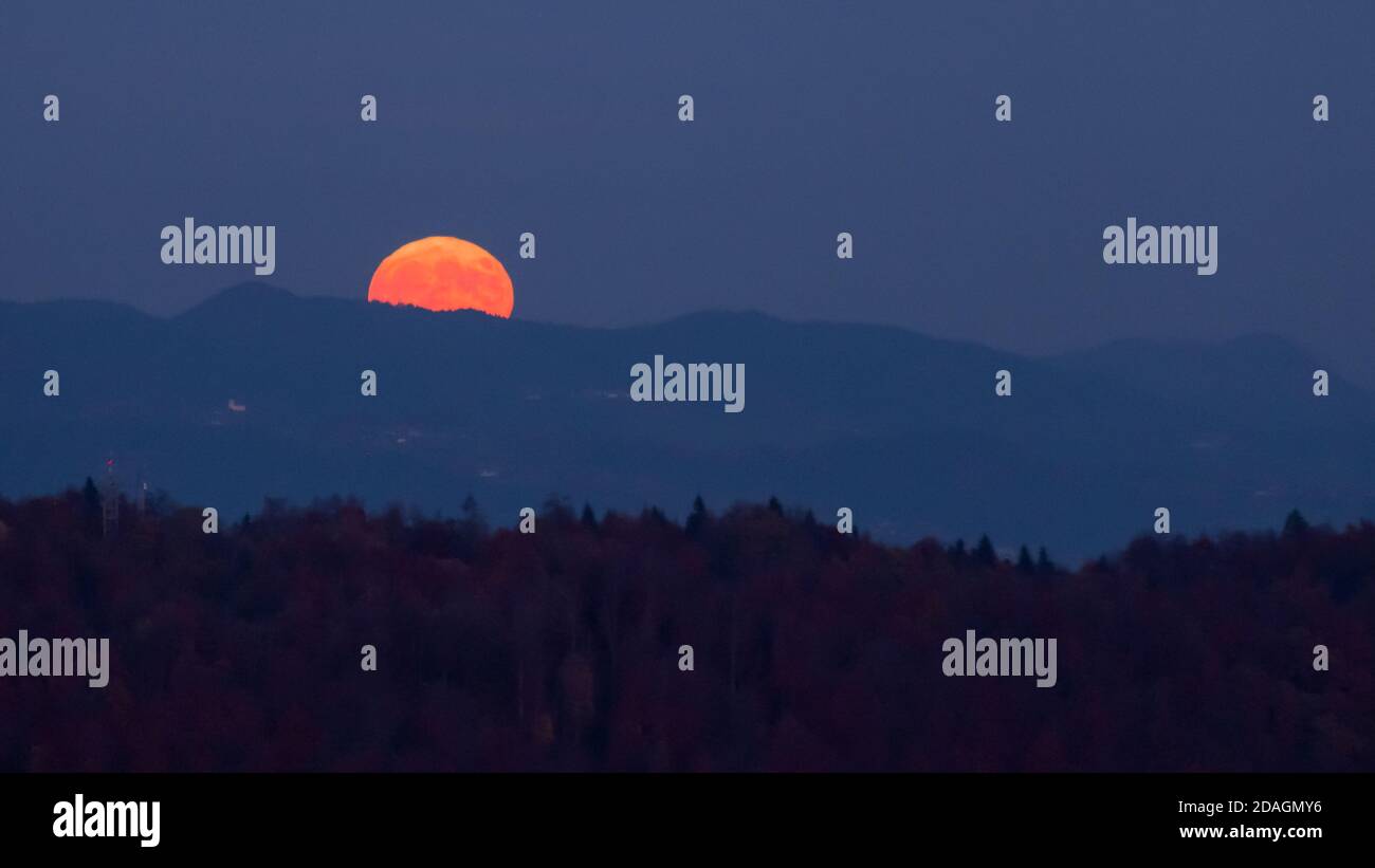 enorme luna piena arancione che si innalza nel cielo notturno alle spalle una cresta di montagna con strati di colline in primo piano creare un'atmosfera mistica Foto Stock