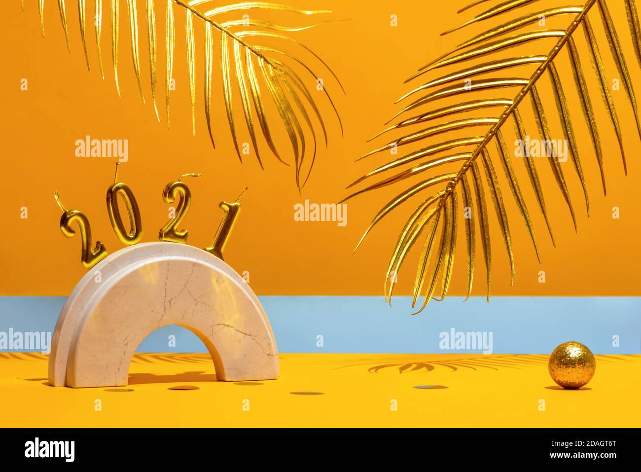 Candele d'oro con il nuovo anno 2021 sull'arco di marmo, foglie di palma, confetti su sfondo giallo con l'orizzonte. Tendenza festiva ancora vita. Foto Stock