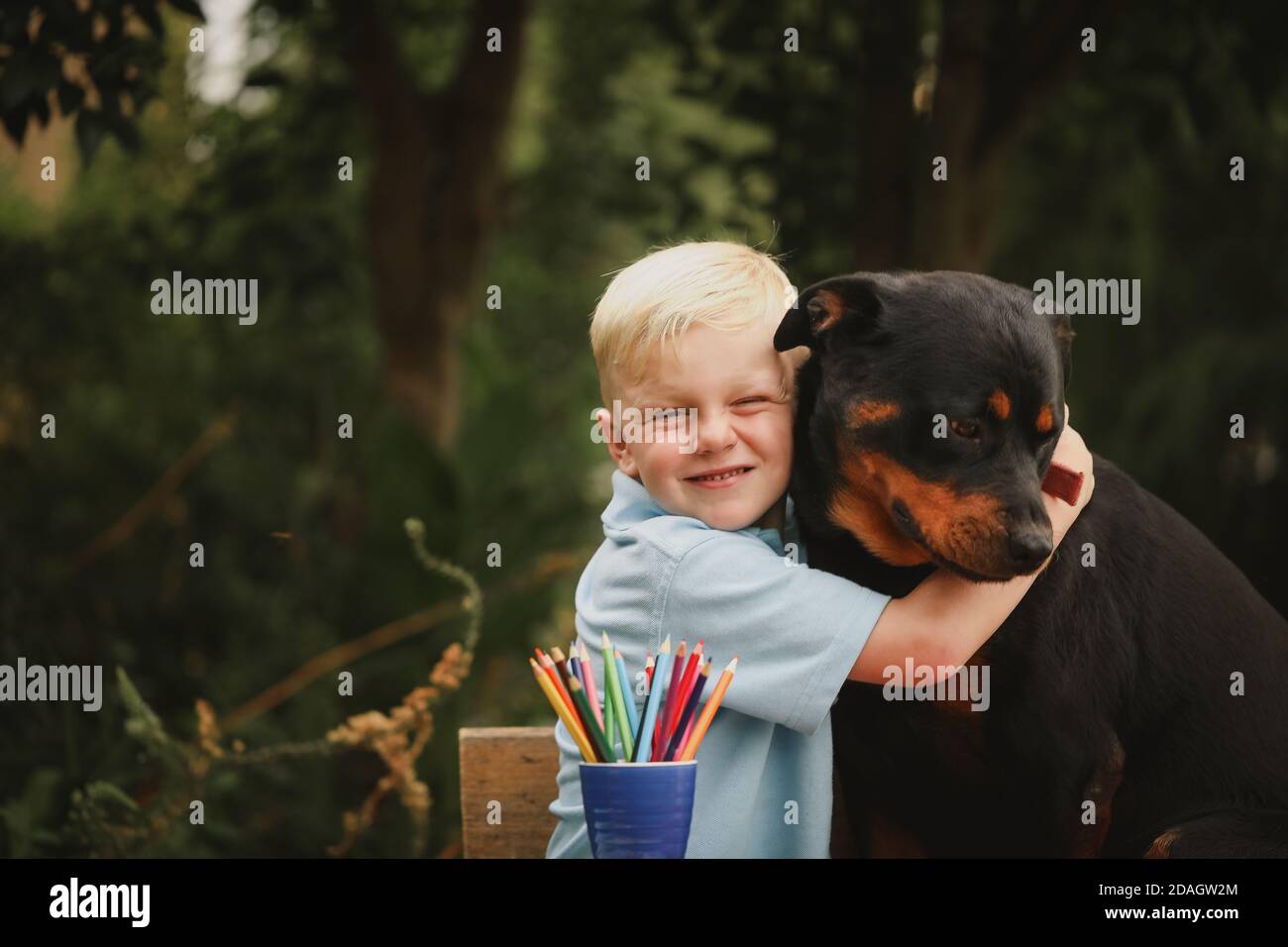 Adorabile ragazzo biondo abbracciando felicemente un grande rottweiler Foto Stock