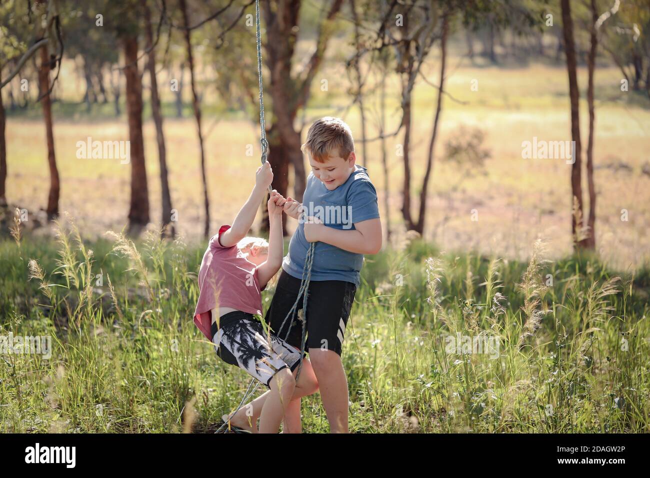 Carino fratelli biondi tirare una corda e giocare felicemente dentro il parco Foto Stock