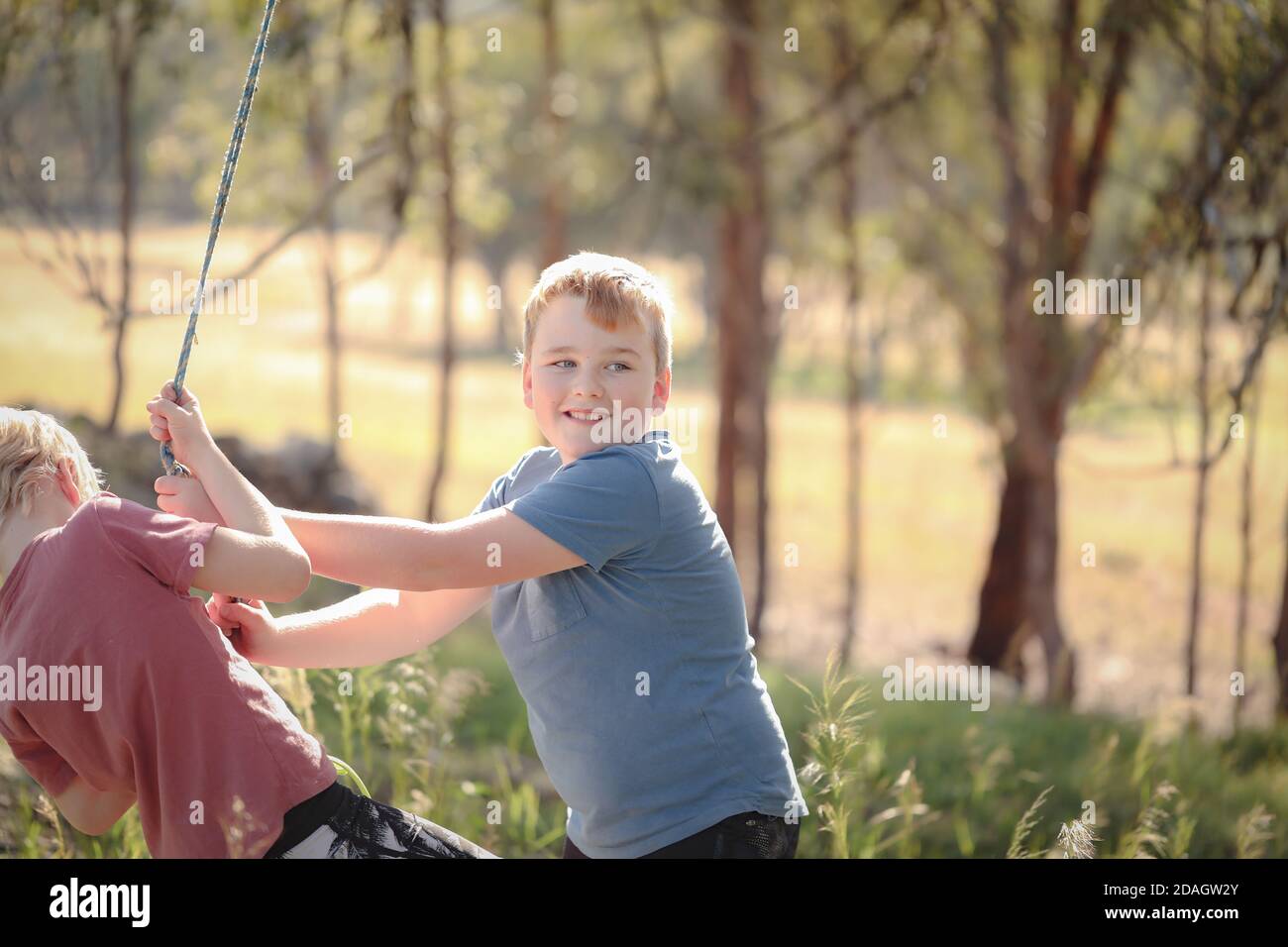 Carino fratelli biondi tirare una corda e giocare felicemente dentro il parco Foto Stock
