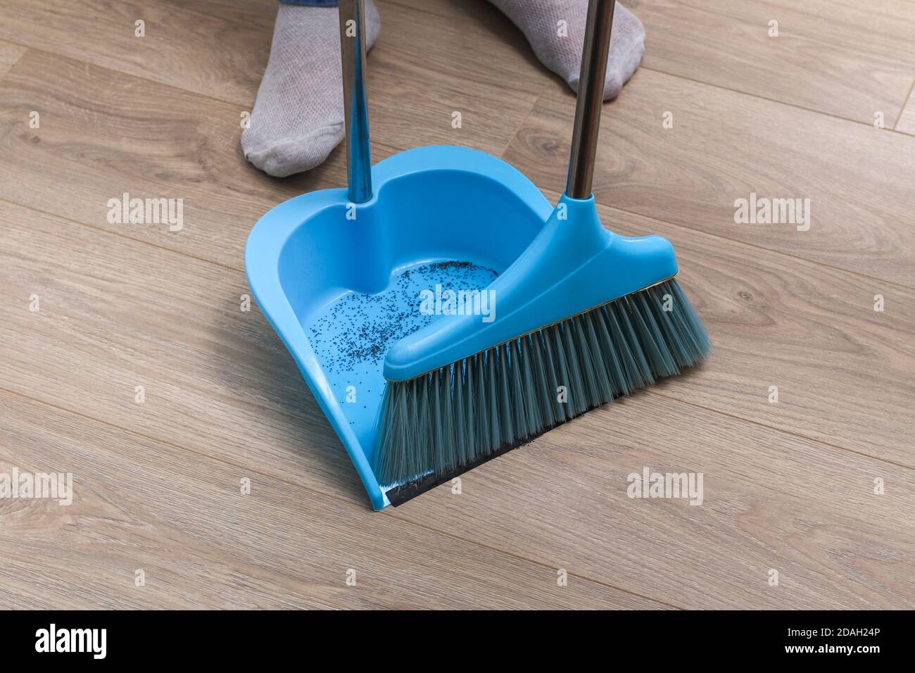 L'uomo spazza i detriti in una paletta blu con una spazzola. Foto Stock