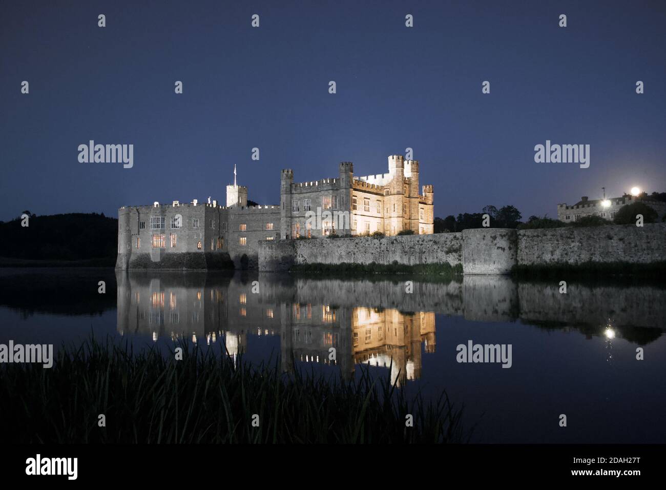 Un antico, tradizionale castello inglese in pietra (Leeds Castle, UK) illuminato di notte e riflesso nelle acque ancora crepuscolari del fossato / lago Foto Stock