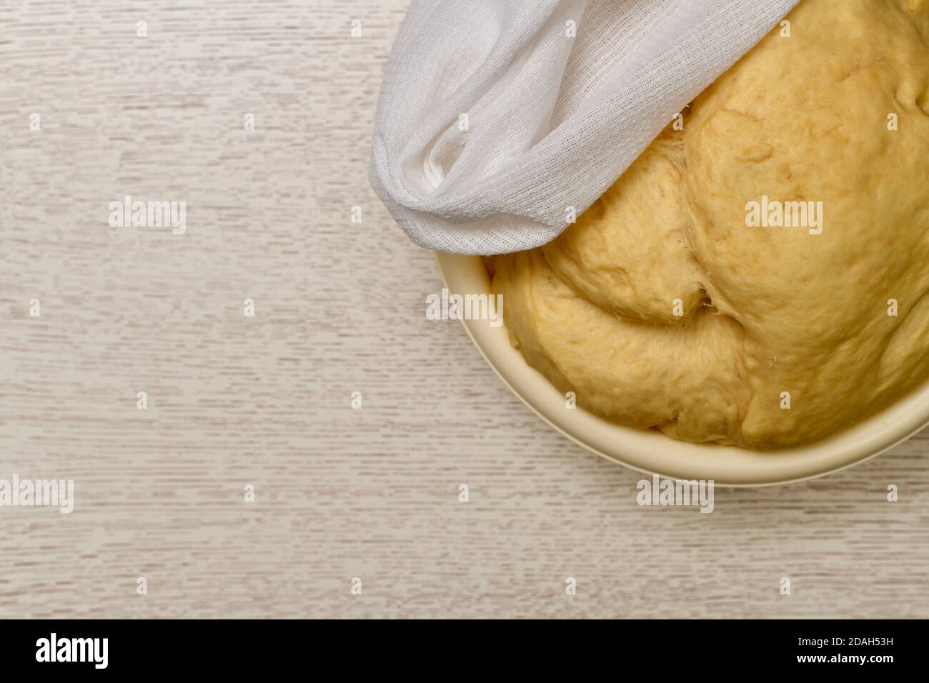 Ciotola con pasta di lievito, coperta con un asciugamano. Sul tavolo si trova la luce sulla destra in alto. Foto Stock