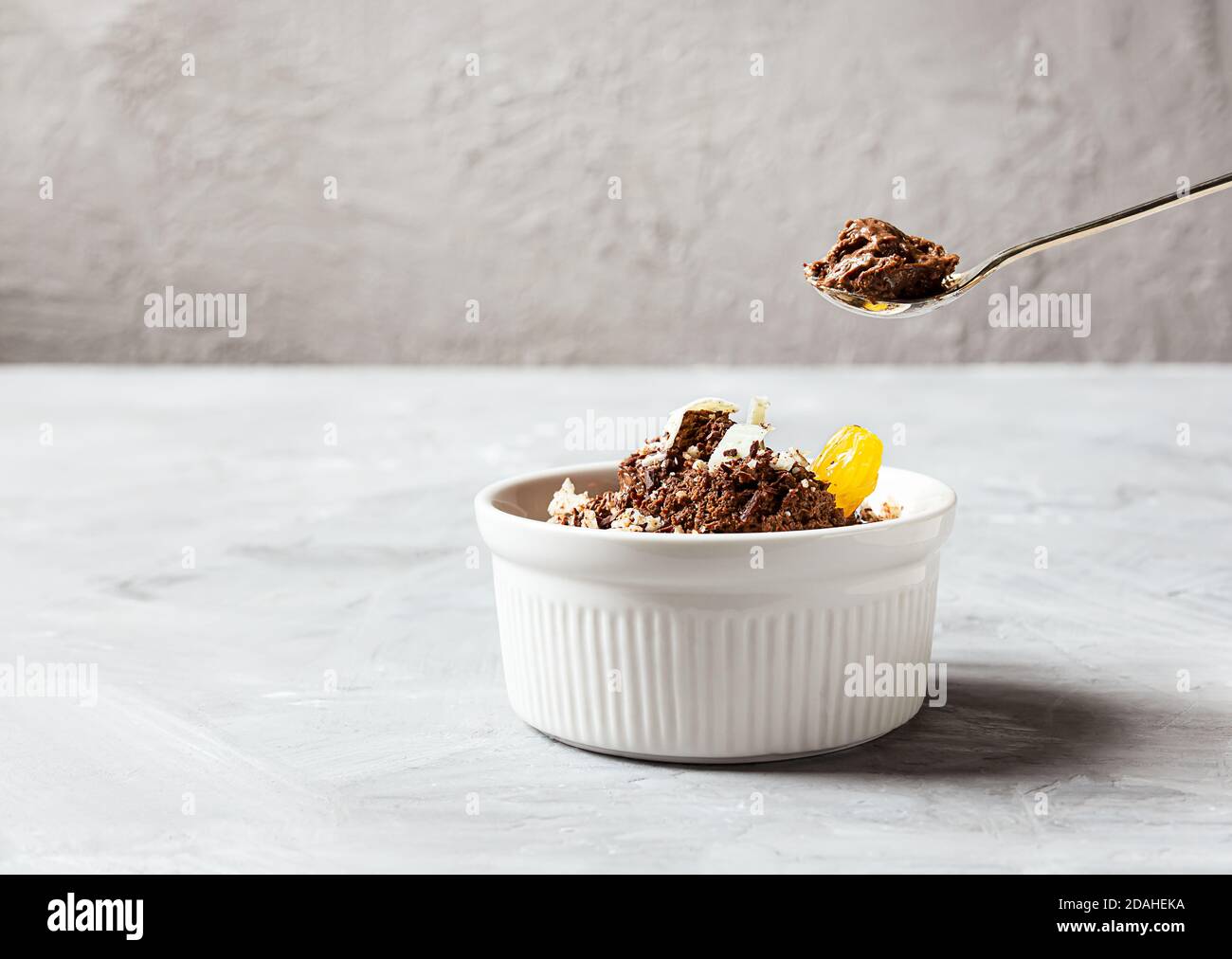 Mousse al cioccolato guarnita con un cuneo di mandarino e scaglie di cioccolato bianco in ciotola bianca e cucchiaino da tè con mousse al cioccolato su sfondo grigio, co Foto Stock