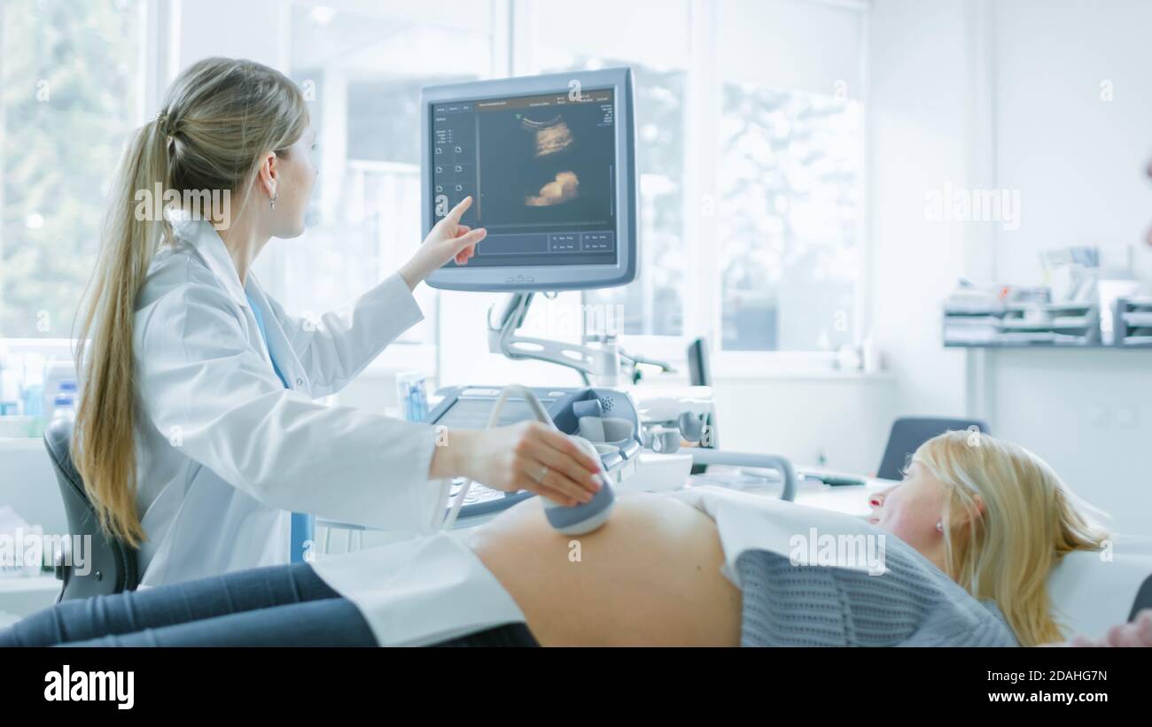 Nell'ospedale, l'ostetrista utilizza il trasduttore per la scansione ecografica dello screening del sonogramma ventaglio della donna incinta e punti il dito sullo schermo Foto Stock