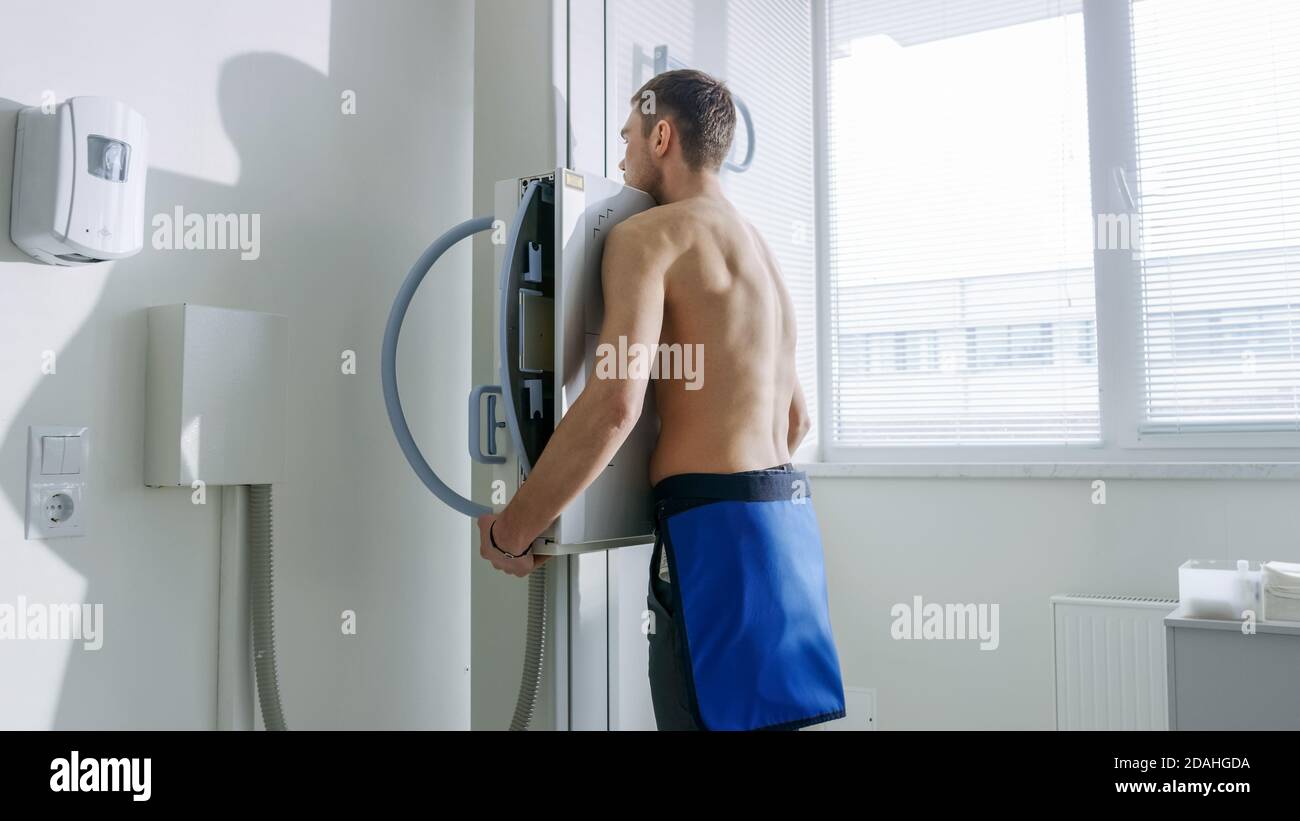 Nell'ospedale, l'uomo in piedi faccia contro il muro mentre la macchina a raggi X lo scansiona. Ricerca di fratture, arti rotti, torace, cancro o tumore. Moderno Foto Stock