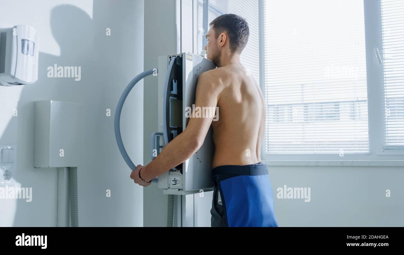 Nell'ospedale, l'uomo in piedi faccia contro il muro mentre la macchina a raggi X lo scansiona. Ricerca di fratture, arti rotti, torace, cancro o tumore. Moderno Foto Stock