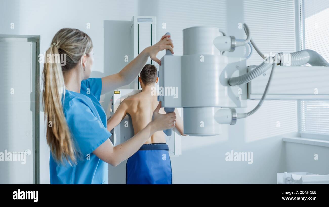 Nell'ospedale, l'uomo in piedi contro il muro, mentre il tecnico medico regola la macchina a raggi X per la scansione. Ricerca di fratture, arti rotti Foto Stock