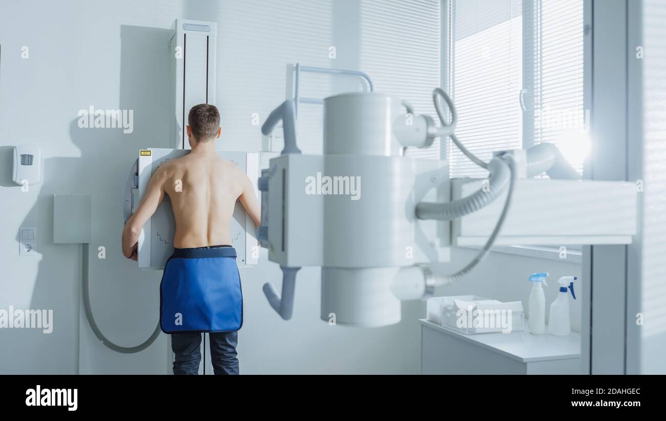 Nell'ospedale, l'uomo in piedi faccia contro il muro mentre la macchina a raggi X lo scansiona. Ricerca di fratture, arti rotti, torace, cancro o tumore. Moderno Foto Stock
