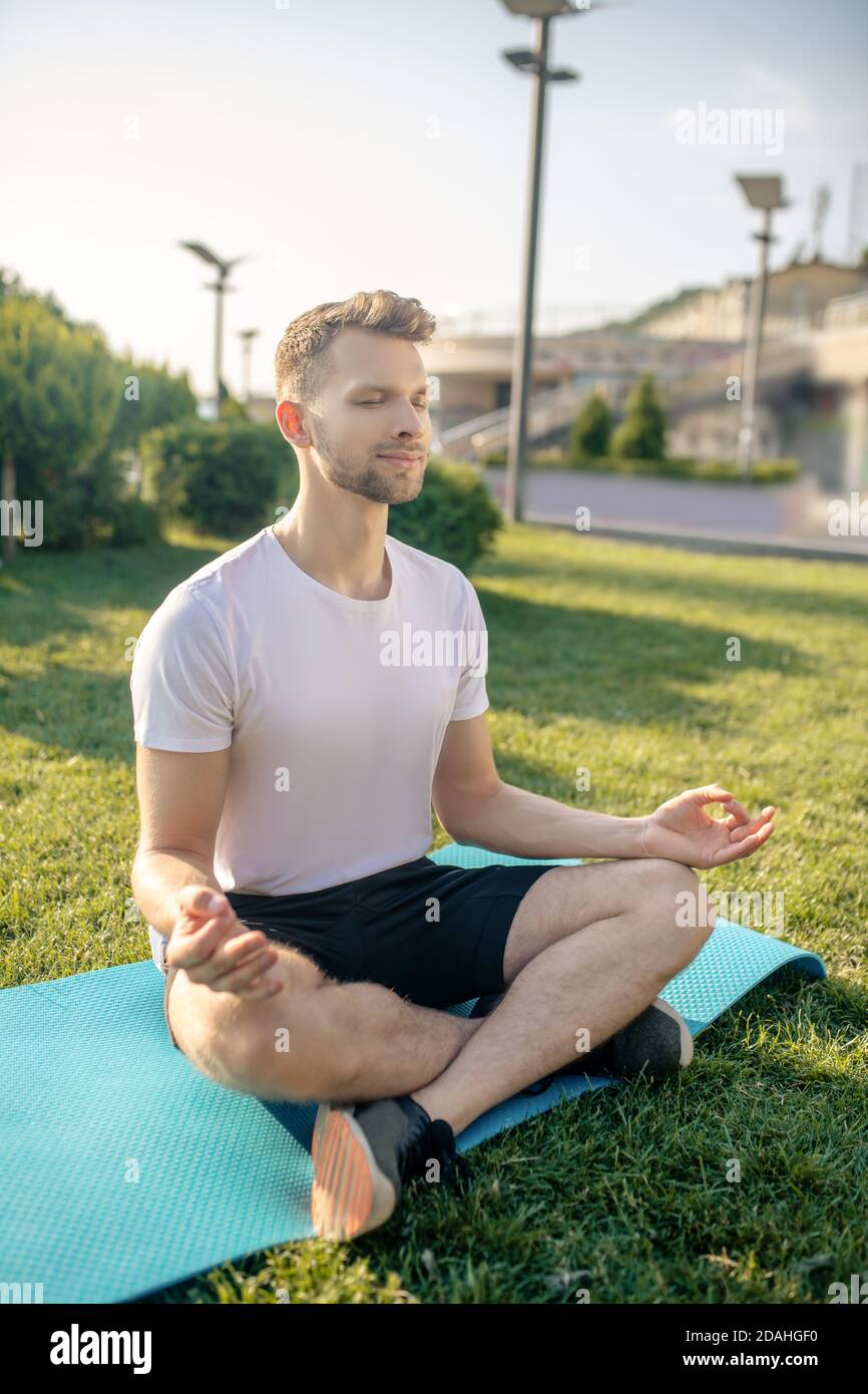Giovane maschio sopportato seduto in loto posa fuori, occhi chiusi, mani in mudra Gyan Foto Stock