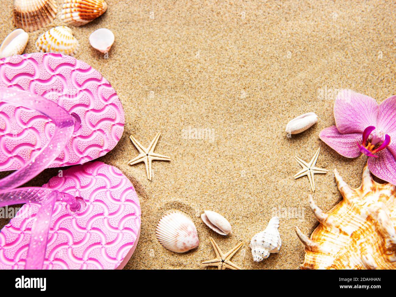 Flip Floops nella sabbia con stelle marine e fiori di orchidee. In estate sulla spiaggia. Spiaggia estiva. Foto Stock