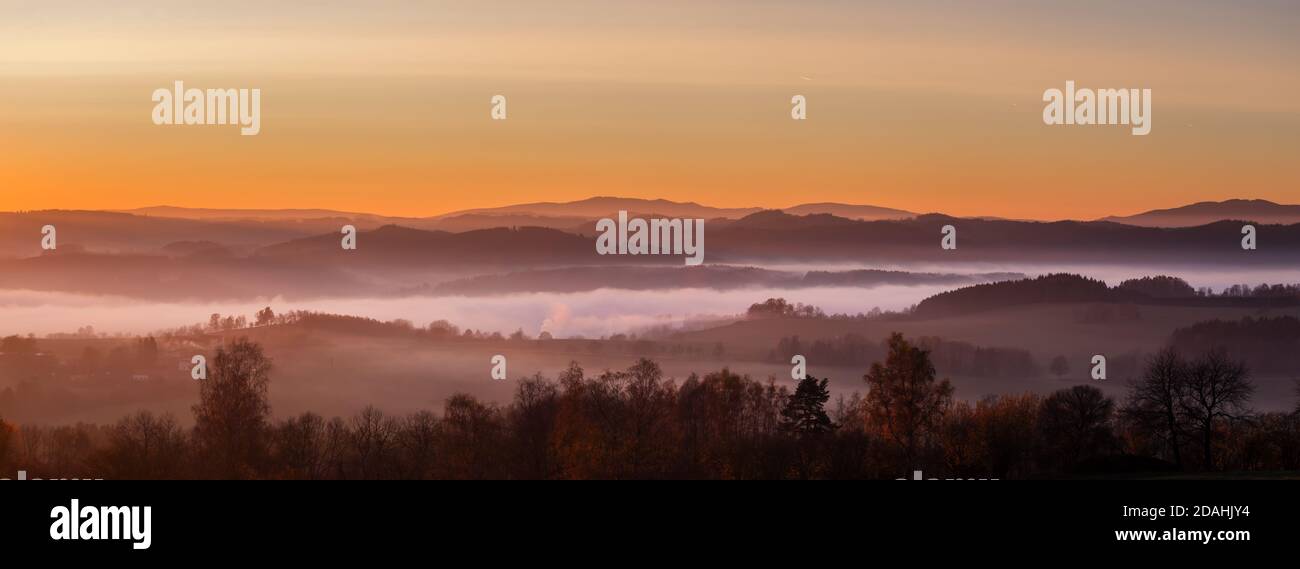 tramonto in montagna - paesaggio collinare con prati e boschi in una foschia, in un cielo giallo e arancione Foto Stock