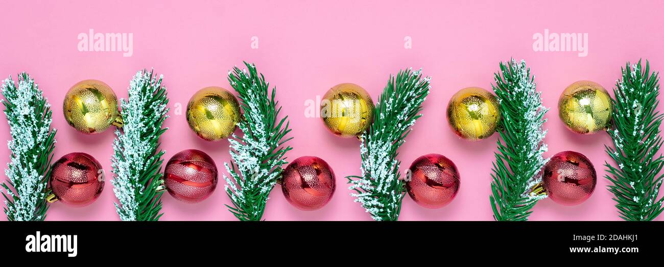 Pinsello natalizio e ciuffi di abete verde, palline scintillanti rosse e dorate su sfondo di carta rosa. Astratto festivo ampio design panoramico. Stagione invernale Foto Stock