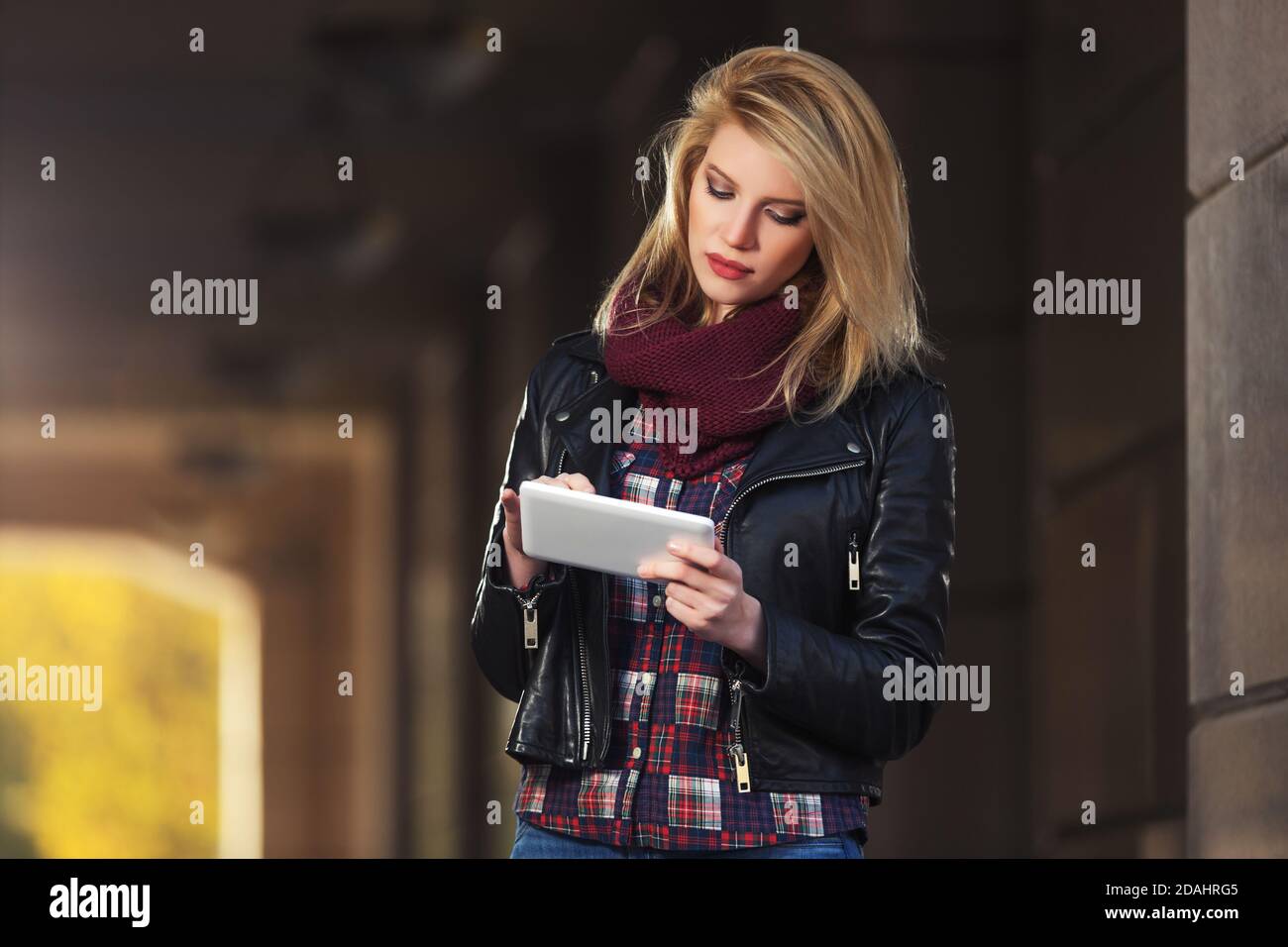 Giovane donna di moda che usa un computer tablet digitale sulla strada della città Elegante modello femminile con giacca in pelle nera e sciarpa snodata Foto Stock