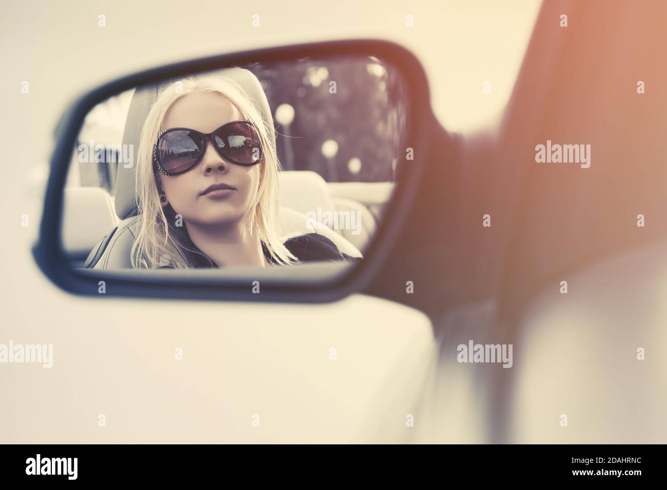 Donna di moda bionda in occhiali da sole guardando nella parte posteriore dell'auto visualizza specchio Foto Stock