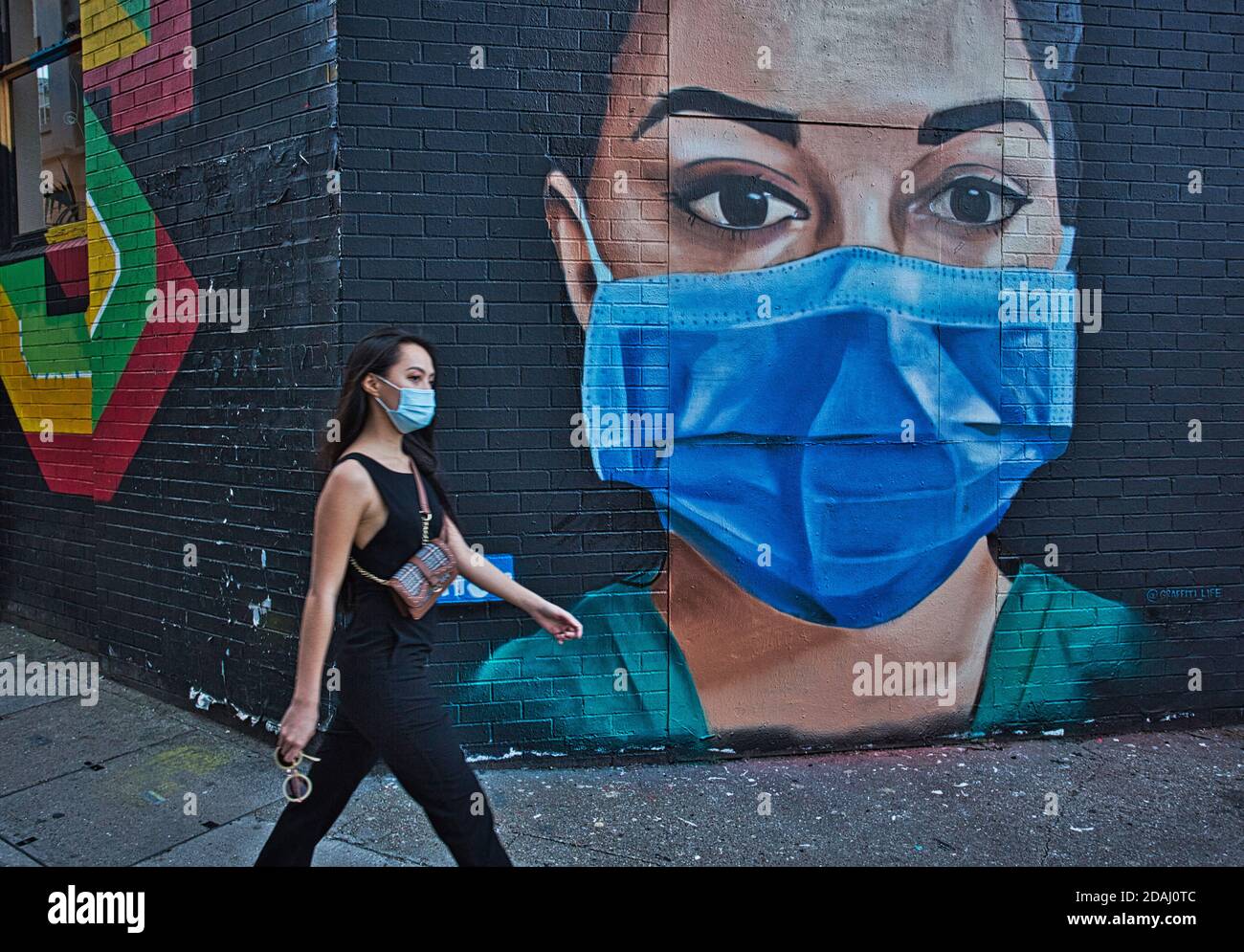 GRAN BRETAGNA / Inghilterra / Londra /UNA donna con maschera facciale cammina oltre un pezzo di Street art raffigurante un infermiere NHS indossando una maschera facciale su 22,04. 2020. Foto Stock
