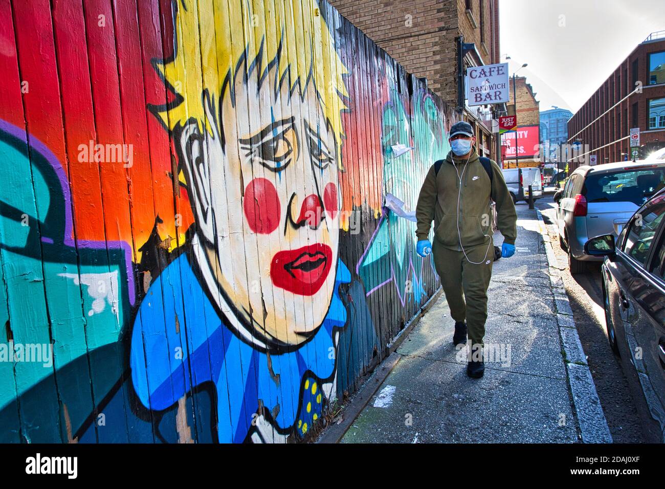 GRAN BRETAGNA / Inghilterra / Londra / UN uomo con maschera cammina oltre i graffiti raffiguranti il primo ministro Boris Johnson come un clown, vicino a Brick Lane . Foto Stock