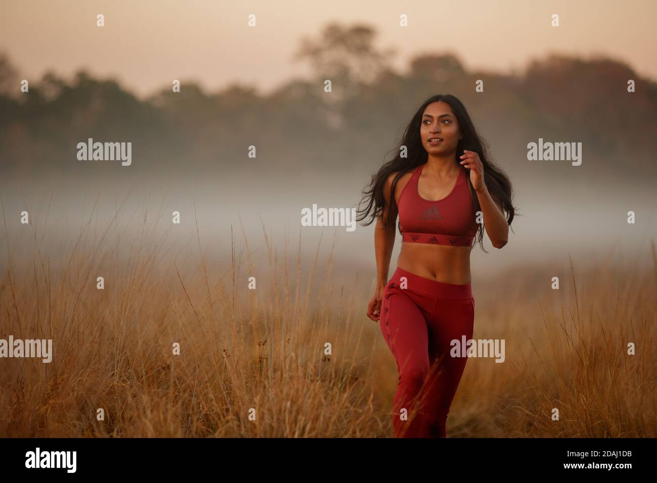 Una donna di discesa asiatica che corre in un parco nebby al tramonto Foto Stock