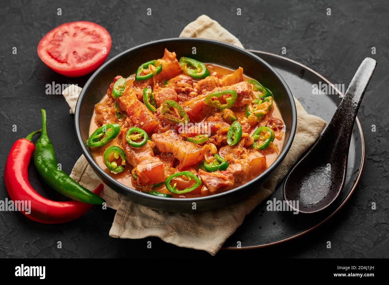 Bicol Express Stew in ciotola nera su tavolo di ardesia scuro. Cucina filippina piccante pancia di maiale cocco latte curry. Cibo asiatico. Foto Stock