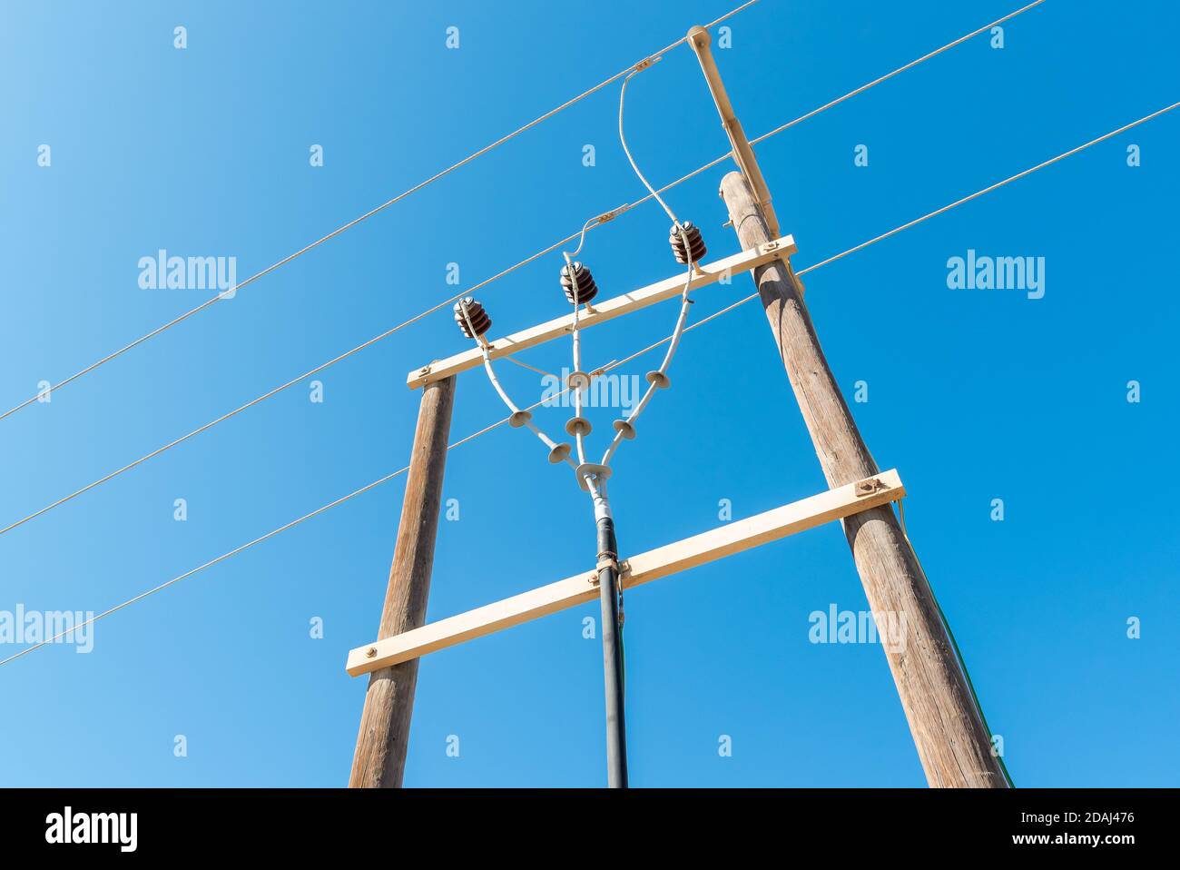 Polo elettrico in legno con fili elettrici ad alta tensione contro cielo blu Foto Stock