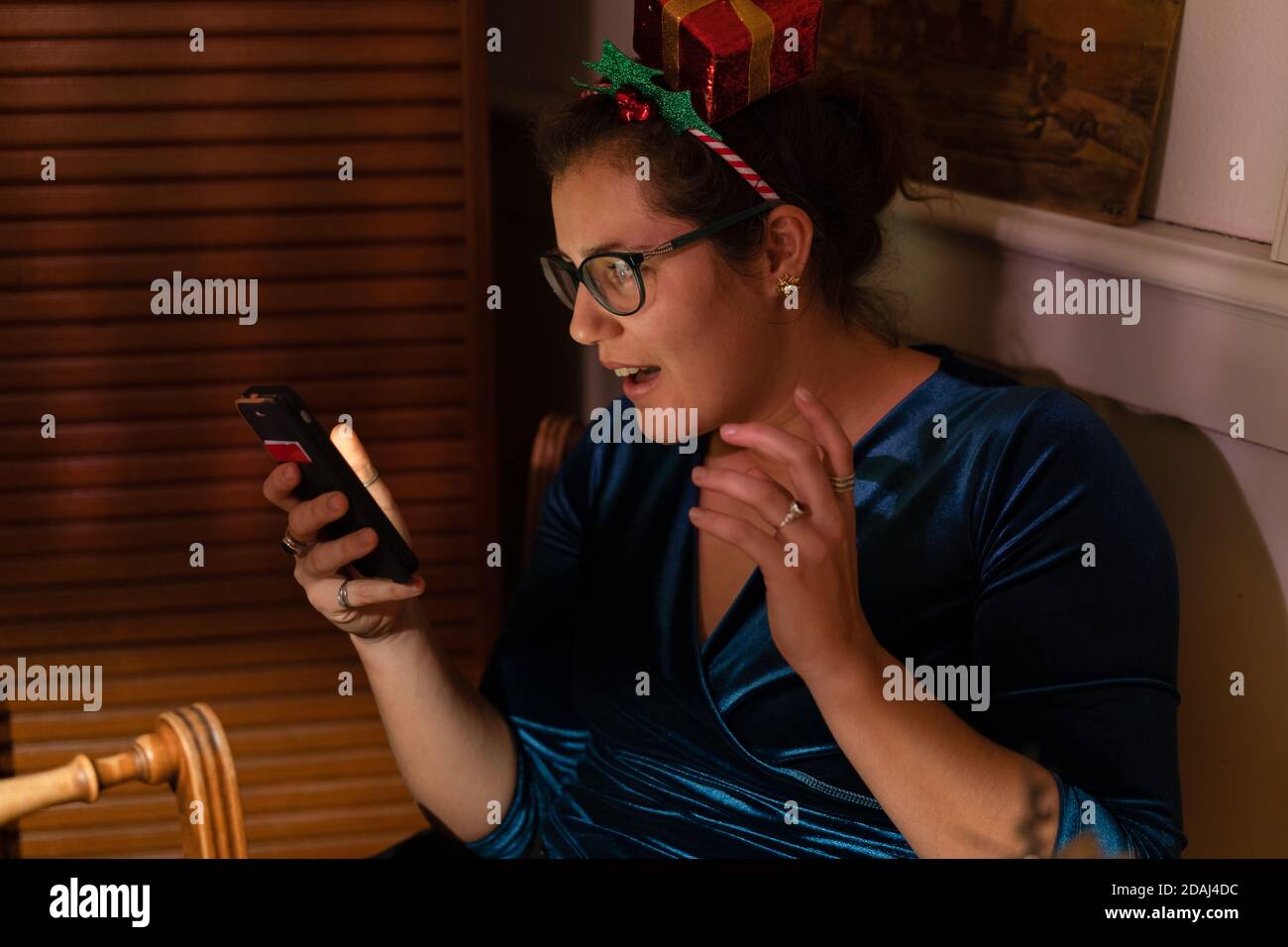 Sorpresa giovane donna con decorazione dei capelli di natale guardando nel suo telefono a natale. Foto Stock